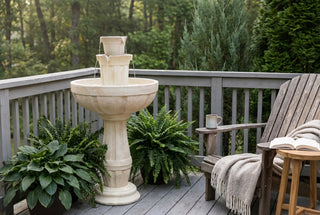 Outdoor setting with a stone fountain, wooden chair, and plants on a deck.