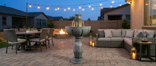 Outdoor patio with seating area, fountain, and string lights at dusk.