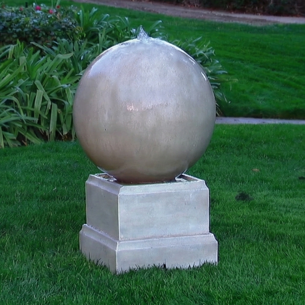 Decorative spherical fountain on a grassy lawn with garden elements in the background
