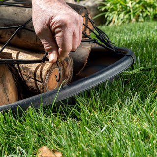 Hand placing a log into a black metal fire pit on grass