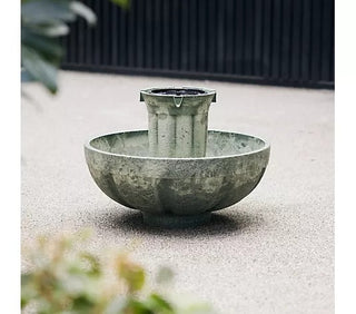 Decorative stone water feature with bowl and spout on a sandy surface