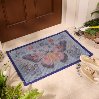 Decorative doormat with cartoon frog design on a tiled floor next to a door.