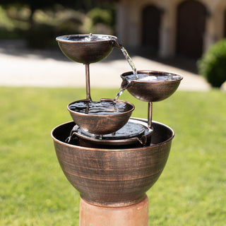 Three-tiered outdoor water fountain with a blurred garden background