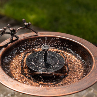 Copper-finished solar water fountain with decorative elements on a blurred green background