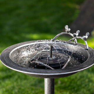 Metallic bird bath with decorative elements on a grassy background