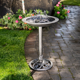 Decorative metal bird bath on a garden path with flowers and grass in the background