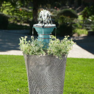 Small garden fountain with plants in a decorative pot on grass