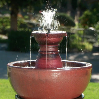 Red ceramic water fountain with water spraying in a garden setting