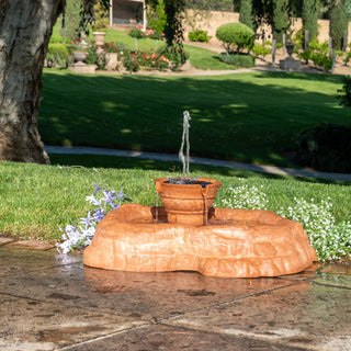 Small stone fountain in a garden with grass and trees in the background