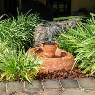 Small garden fountain surrounded by green plants on a stone patio