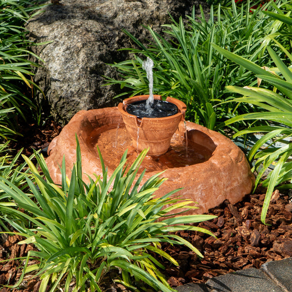 Small terracotta garden fountain surrounded by green plants