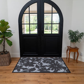 Floral patterned rug in front of a black double door with plants on either side.