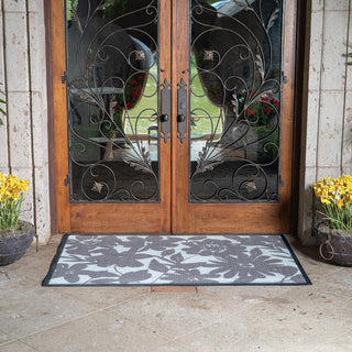 Decorative doormat with floral pattern in front of a wooden door with glass panels.